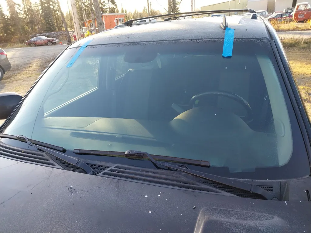 Replacement windshield installed in a dark SUV with blue retaining tape at the roofline