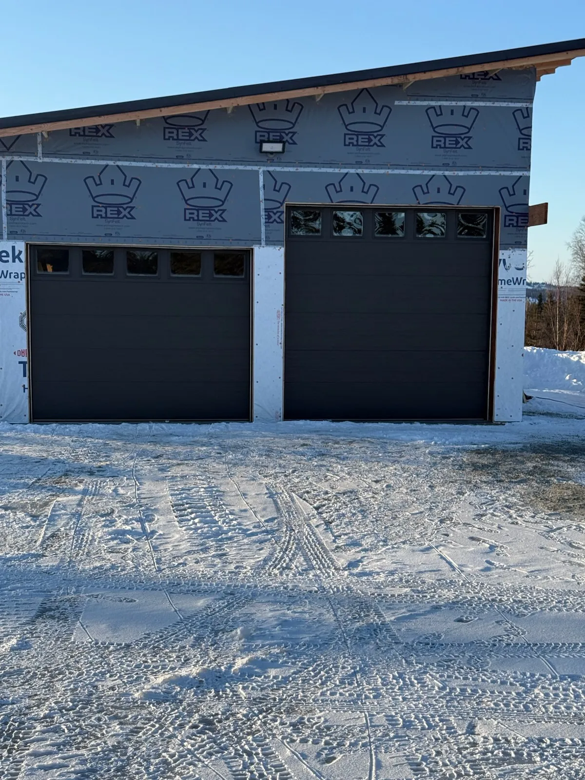 Two dark garage doors on a new building with snow covering the driveway