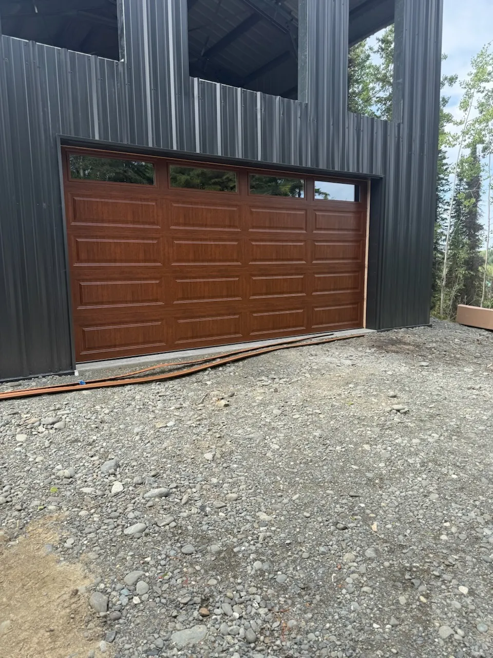 Wood-finish garage door installed in a dark metal-sided building