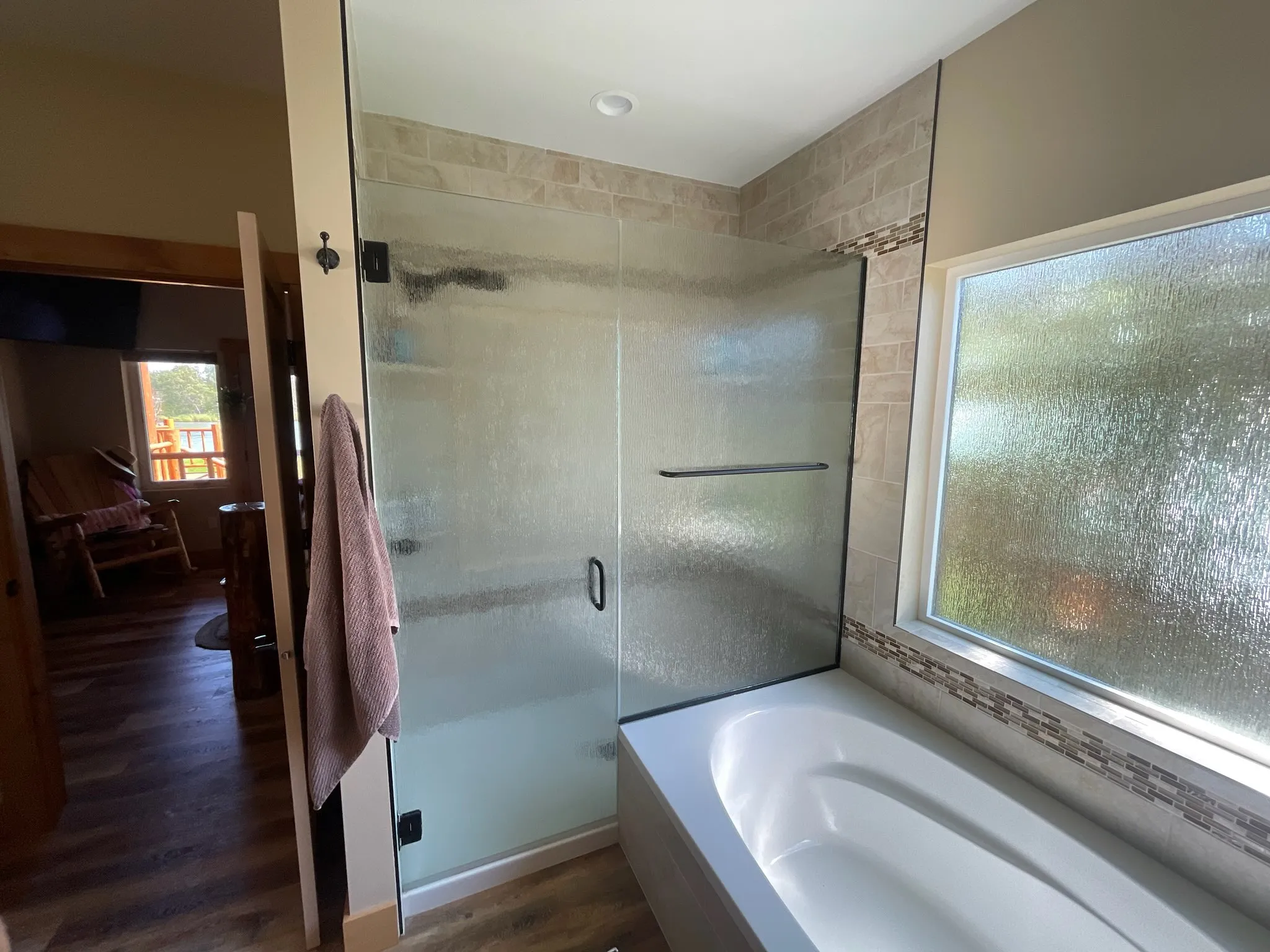 Textured glass shower enclosure with dark hardware beside a white soaking tub