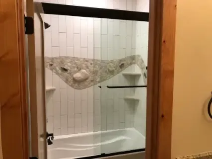 Glass shower enclosure installed above a white bathtub with decorative tile
