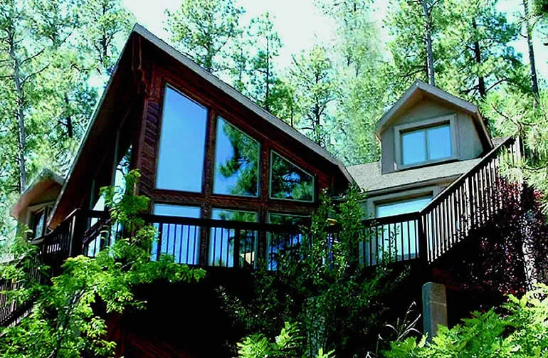 Home exterior with multiple large residential windows surrounded by trees